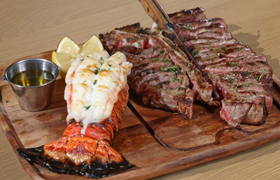 t-bone steak and a juicy lobster tail with butter sauce and lemon on the side